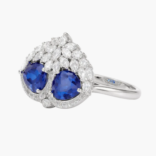 Ring with two blue gemstones and diamond-studded halo on a white background