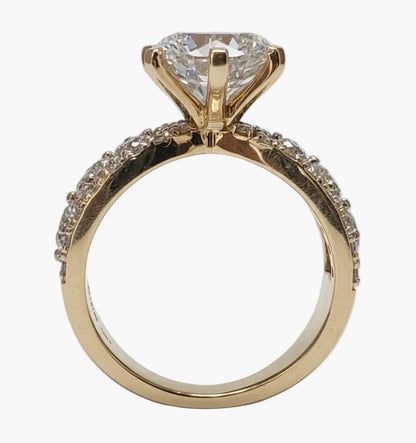 Gold ring with a large diamond and smaller diamonds on the band against a light gray background